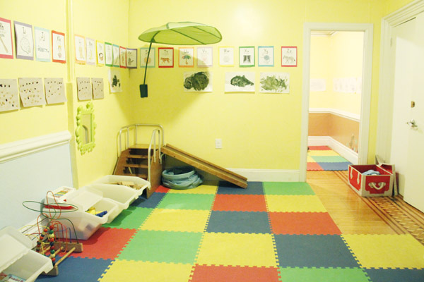 Archival playroom photo with floor mats, play equipment, and a leaf canopy